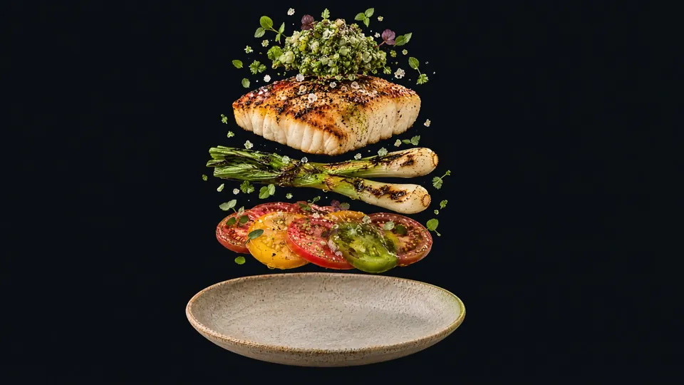 An oak-fired halibut plate lifted apart into layers: salsa verde, the halibut fillet, grilled spring onions, heirloom tomato slices and the stoneware plate.